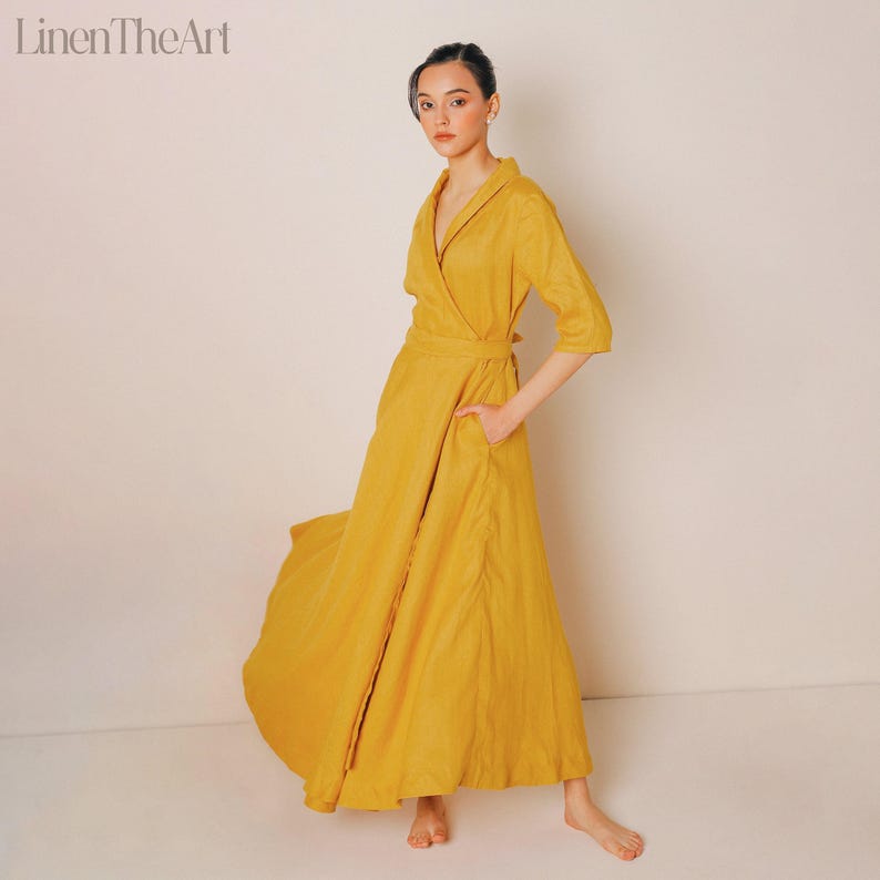 A woman wearing a long, yellow dress with a wrap-style neckline and a high collar, posing against a plain white background.