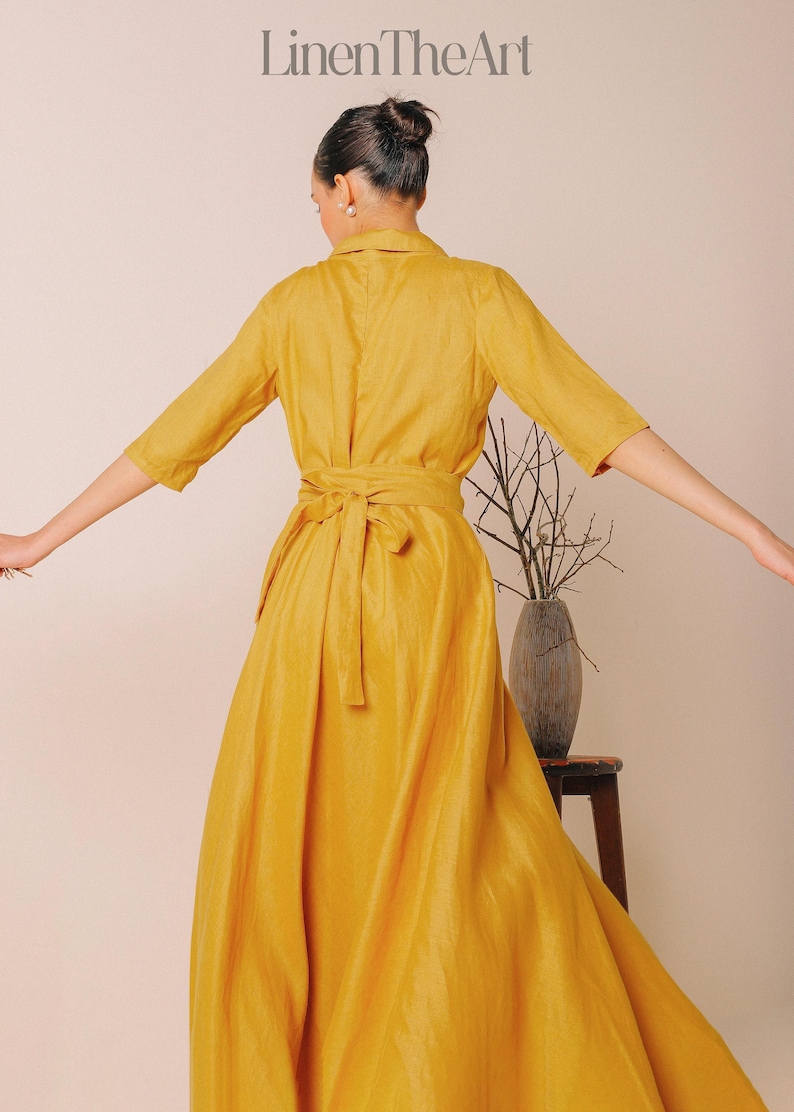 A woman in a long yellow dress stands with her arms outstretched, facing away from the camera.