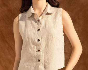 May include: A sleeveless, button-down top in a neutral beige color. The top has a collared neckline and dark brown buttons. The fabric appears to be linen or a similar lightweight material. The top is part of a matching set.