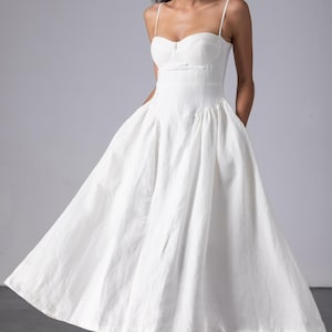 May include: A white dress with a fitted bodice and a full, flowing skirt. The dress features thin spaghetti straps and a sweetheart neckline. The fabric appears to be a lightweight material, suitable for warmer weather. The dress is knee-length.