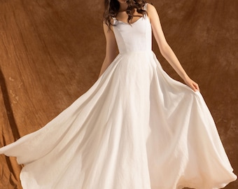 May include: A white, floor-length dress with a fitted bodice and flowing skirt. The dress features a sweetheart neckline and spaghetti straps. The fabric appears to be a lightweight linen or cotton, ideal for a summer event.
