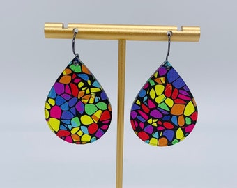 May include: A pair of teardrop-shaped earrings with a colorful mosaic pattern on a black background. The earrings are hanging from a gold stand.