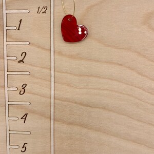 May include: A wooden growth chart with a red heart hanging from a gold ring. The chart has markings for inches, with numbers 1 through 6.