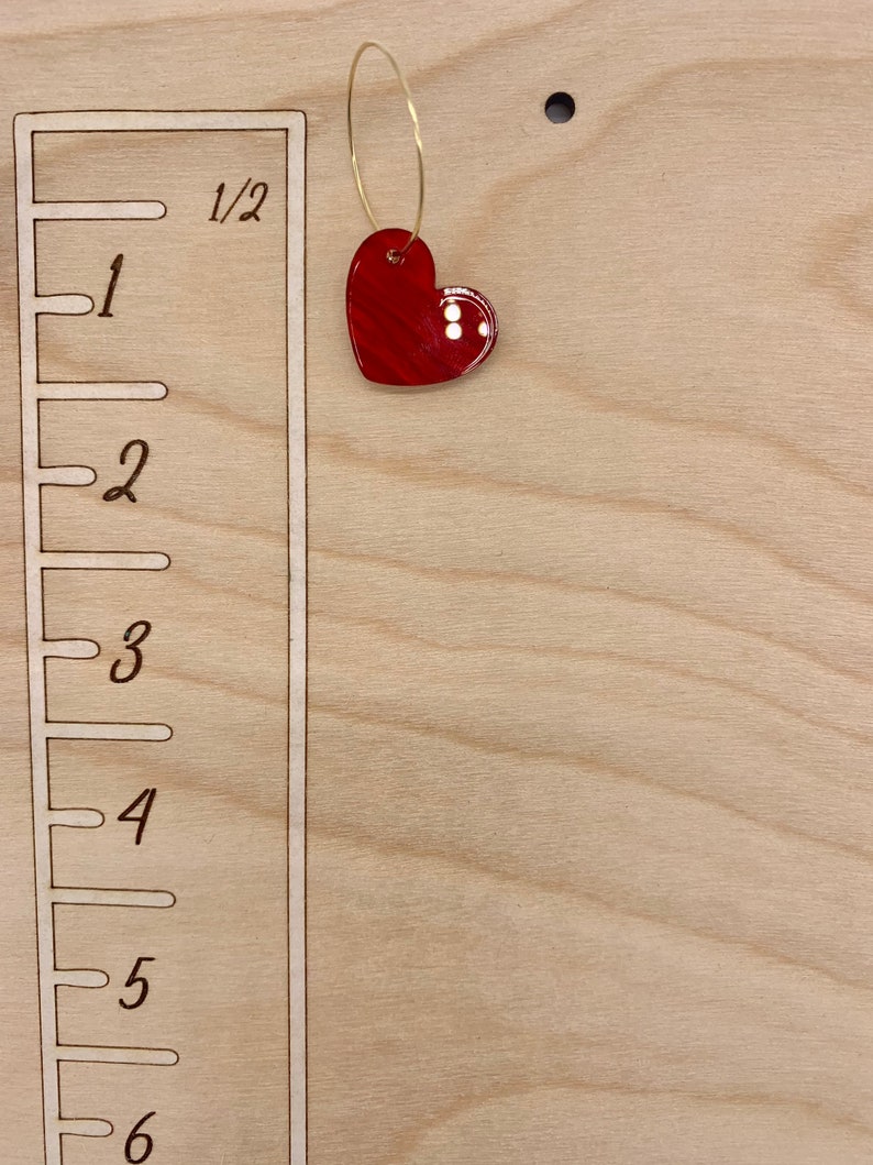 May include: A wooden growth chart with a red heart hanging from a gold ring. The chart has markings for inches, with numbers 1 through 6.
