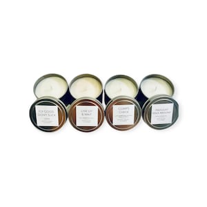 May include: Four silver candle tins with white lids. The lids have black labels with white text. The labels read "Fly Good, Don't Suck", "Line Up & Wait", "Gumps Check", and "Preflight Walk Around".