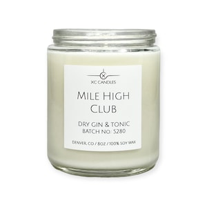 May include: A clear glass jar candle with a white label that reads "XC CANDLES", "MILE HIGH CLUB", "DRY GIN & TONIC", "BATCH NO: 5280", and "DENVER, CO/8OZ/100% SOY WAX".