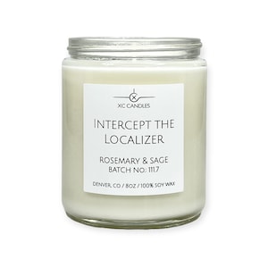 May include: A white candle in a clear glass jar with a white label. The label reads "XC CANDLES", "INTERCEPT THE LOCALIZER", "ROSEMARY & SAGE", "BATCH NO.: 111.7", and "DENVER, CO/8OZ/100% SOY WAX".