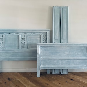 May include: A light blue wooden headboard with intricate carvings and a matching footboard. The headboard is taller than the footboard and has a more ornate design.