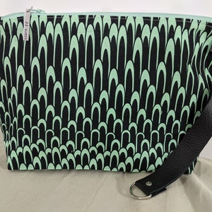 May include: A black and green zippered pouch with a black leather strap and silver hardware. The pouch has a repeating pattern of green arches on a black background. The pouch has a tag that says "Sewing PP".