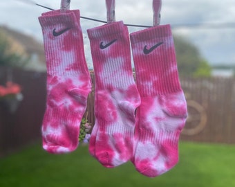 Puede incluir: Tres calcetines de color rosa y blanco con el logotipo de Nike en negro colgados de una cuerda para tender la ropa.