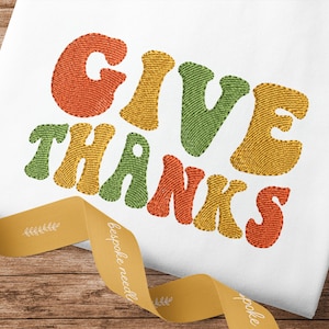 May include: Embroidered "Give Thanks" text in a retro style with orange, yellow, and green colors on a white fabric background.