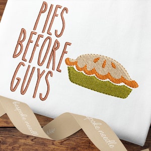 Puede incluir: Diseño bordado en una bolsa de tela blanca con el texto "PIES BEFORE GUYS" en hilo marrón y una tarta bordada en verde y naranja.