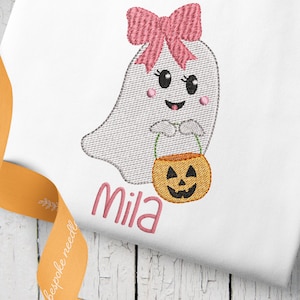 Puede incluir: Diseño bordado de un lindo fantasma con un lazo rosa, sosteniendo un cubo de calabaza. El nombre "Mila" está bordado debajo del fantasma.