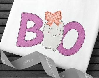 May include: A white fabric with the word "BOO" embroidered in pink with a white ghost with a pink bow in the middle. The letters are pink with white polka dots.