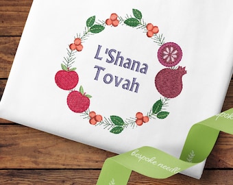 May include: Embroidered design featuring a wreath of green leaves, red berries, apples, and a pomegranate. The wreath surrounds the text "L'Shana Tovah".