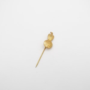 May include: A gold-colored stick pin with an eagle-shaped top. The pin has a round base with the text "RACINE USA" and a long, slender needle. The pin is likely a vintage or collectible item.