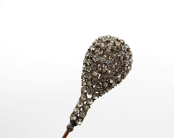 May include: A silver-toned hat pin with a teardrop-shaped head covered in clear rhinestones.