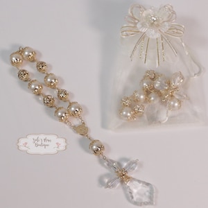 May include: A white pearl rosary with a gold-toned chain and a crystal cross. The rosary is in a white organza bag with a gold bow.