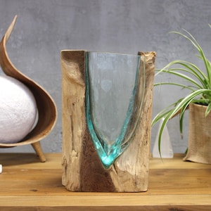 Peut inclure: Un récipient en verre transparent en forme de goutte d'eau, inséré dans un morceau de bois brut et naturel de couleur brun clair. Le verre présente une légère teinte bleu-vert et épouse les contours organiques et irréguliers du bois.