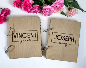 May include: Two wooden photo albums with ring binders. The album on the left has the name "VINCENT" and the name "jacob" written underneath. The album on the right has the name "JOSEPH" and the name "corey" written underneath.
