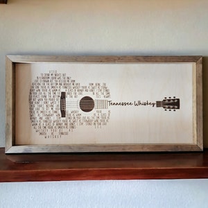 May include: A framed wood sign with a laser-etched image of a guitar and the lyrics to the song "Tennessee Whiskey" by Chris Stapleton. The lyrics include the lines "You're as smooth as Tennessee Whiskey" and "I'll always love you."