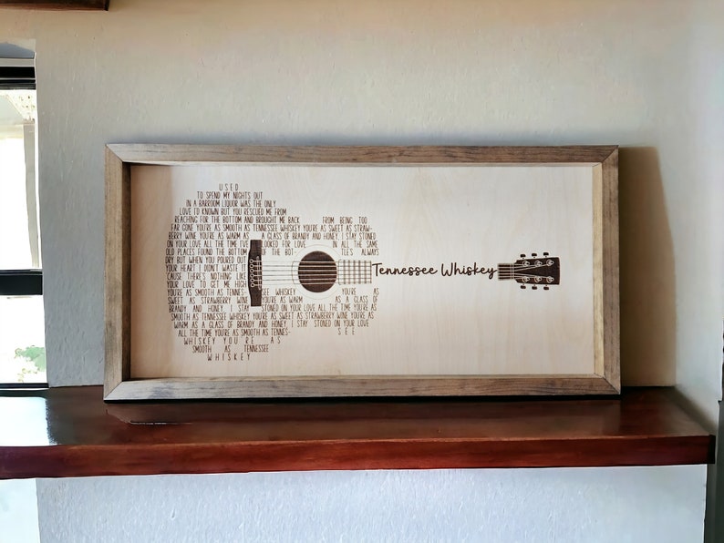 May include: A framed wood sign with a laser-etched image of a guitar and the lyrics to the song "Tennessee Whiskey" by Chris Stapleton. The lyrics include the lines "You're as smooth as Tennessee Whiskey" and "I'll always love you."