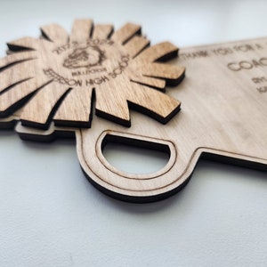 May include: A wooden plaque with the text "Thank you for a great season Coach White" and a list of names. The plaque is shaped like a school bus and has a wooden flower with the text "2022-2023 Jefferson High School Bulldogs" on it.