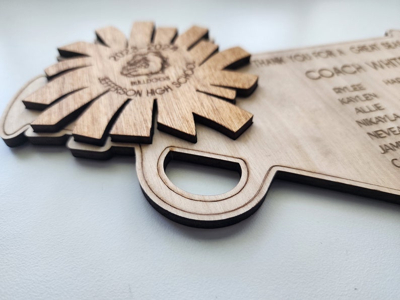May include: A wooden plaque with the text "Thank you for a great season Coach White" and a list of names. The plaque is shaped like a school bus and has a wooden flower with the text "2022-2023 Jefferson High School Bulldogs" on it.