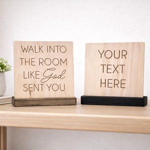May include: Two wooden signs with engraved text. One says "WALK INTO THE ROOM LIKE God SENT YOU" and the other says "YOUR TEXT HERE". Both signs are on a wooden surface with a small plant and a pencil holder.