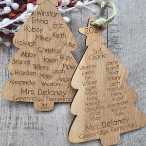 May include: Two wooden Christmas tree ornaments with the year 2024 at the top. The ornaments are decorated with the names of students and the teacher, "Mrs. Delaney", and the school name, "Greenridge Elementary".