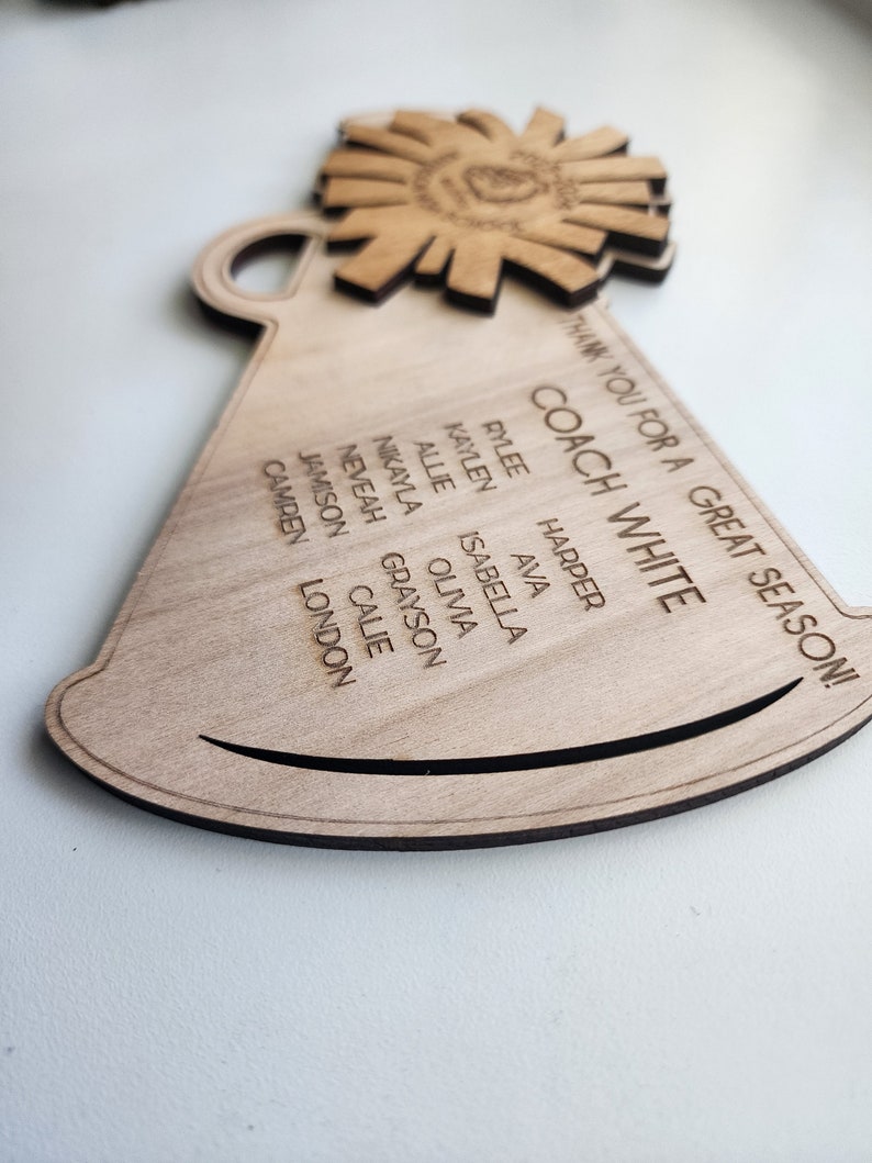 May include: A wooden megaphone with the text "THANK YOU FOR A GREAT SEASON! COACH WHITE" and a list of names: Rylee, Harper, Kaylen, Ava, Allie, Isabella, Nikayla, Olivia, Neveah, Grayson, Jamison, Calie, Camren, London.
