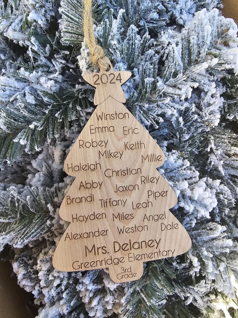 May include: A wooden Christmas tree ornament with the year 2024 at the top and a list of names, including "Mrs. Delaney, Greenridge Elementary, 3rd Grade".