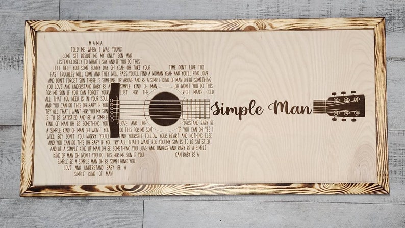 May include: A wooden sign with a burnt orange frame features the lyrics to the song "Simple Man" by Lynyrd Skynyrd. The lyrics are printed in a brown font and the sign includes a silhouette of an acoustic guitar.