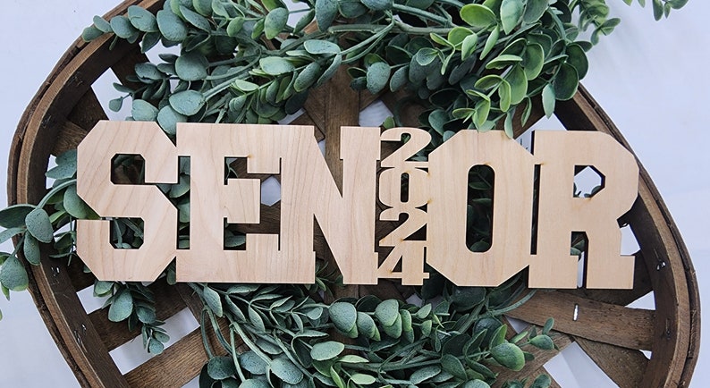 May include: Wooden sign with the word "SENIOR" and the year "2024" in large, block letters. The sign is light brown and has a rustic look.