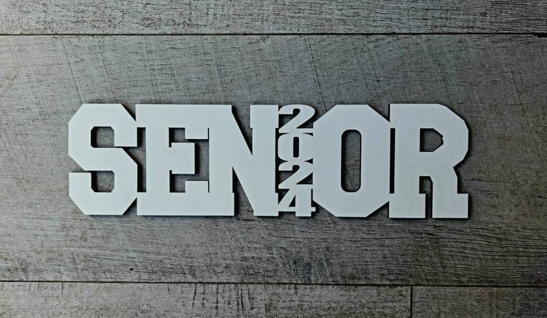 May include: White wooden sign with the word "SENIOR" in large, bold letters and the year "2024" in smaller letters.