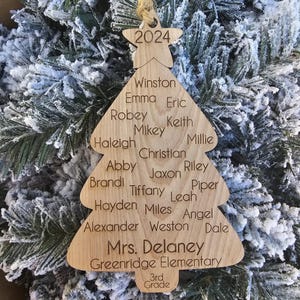 May include: A wooden Christmas tree ornament with the year 2024 at the top. The ornament is decorated with the names of students and the teacher, "Mrs. Delaney", and the school name, "Greenridge Elementary". The ornament also includes the grade, "3rd Grade".