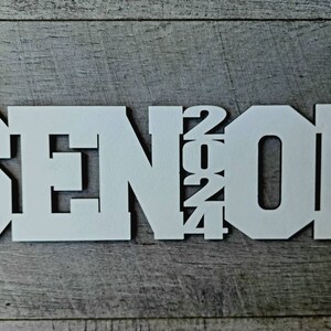 May include: White wooden sign with the word "SENIOR" and the year "2024" in a layered design.