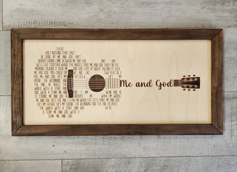 May include: A wooden sign with a brown frame and a laser-etched design of a guitar and lyrics. The lyrics read "There ain't nothing that can't be done by me and God, ain't nobody gonna come between me and God. One day we'll live together where the angels trod, me and God, early in the morning talking it over, me and God, late at night talking it over. We are like two peas in a pod, me and God. He's my father, the beginning and the end, he rules the world with a staff and rod. We're a team, me and God. I am weak and he is strong, me and God. He forgives me when I'm wrong. He's my father, he's my friend, the beginning and the end, he rules the world with a staff and rod. We're a team, me and God."