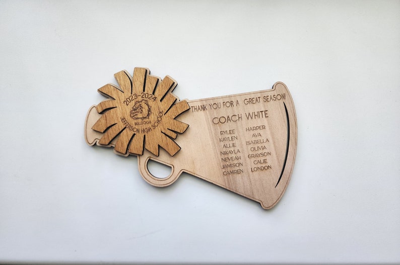 May include: A wooden megaphone with a starburst design on the top. The megaphone has the text "Thank you for a great season! Coach White" and a list of names.