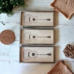 May include: Three wooden framed prints with a guitar silhouette made of song lyrics. The prints feature the text "Tennessee Whiskey", "Thank God", and "Me and God".