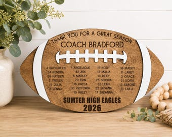 May include: A wooden football-shaped plaque with white painted accents. The text reads THANK YOU FOR A GREAT SEASON, COACH BRADFORD, SUMTER HIGH EAGLES, 2026, and lists player names with jersey numbers including Brooklyn, Angelique, Kody, and Maddy.