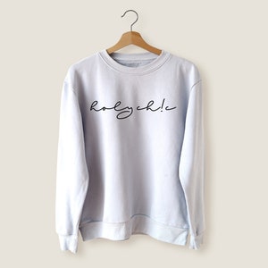 Puede incluir: Una sudadera de color azul claro con el texto "holy chic!" impreso en negro en la parte delantera.