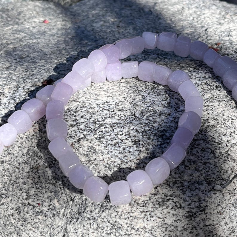 Pu&ograve; includere: Una collana di perline cubiche di colore viola chiaro semitraslucido disposte in un motivo circolare. Le perline hanno una finitura liscia e lucida e sono infilate insieme, creando un anello continuo di unit&agrave; quadrate uniformi color lavanda.