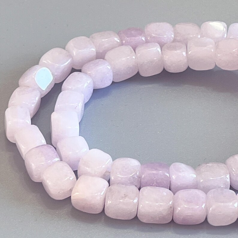 Pu&ograve; includere: Una fila di perline a forma di cubo color lavanda chiaro con una finitura liscia e lucida. Le perline sono disposte in una linea curva, mettendo in risalto la loro forma quadrata uniforme e il delicato colore viola traslucido dell'intera fila.
