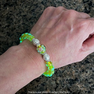 May include: A neon green beaded bracelet with decorative silver beads and clear, round beads. Some beads have a swirl design. The bracelet is on a wrist. The bracelet is made of glass beads.