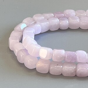 Pu&ograve; includere: Una fila di perline cubiche color viola chiaro con una finitura liscia e lucida. Le perline sono disposte in una linea curva, mettendo in risalto la loro forma quadrata uniforme e la delicata tonalit&agrave; lavanda, con riflessi di luce.
