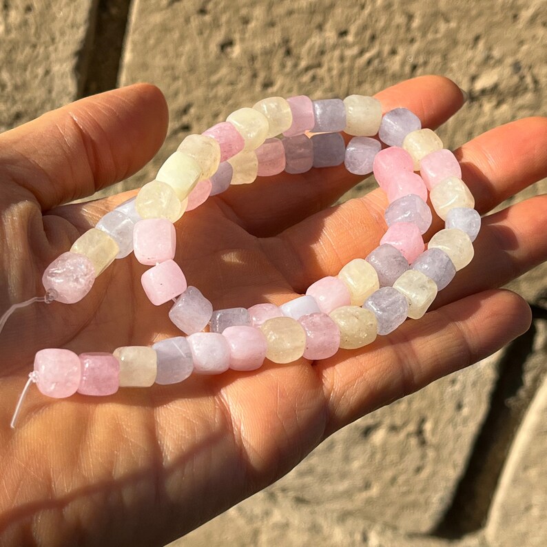 Peut inclure: Un fil de perles carr&eacute;es de couleur pastel dans les tons de rose, de lavande et de jaune. Les perles sont enfil&eacute;es sur un fin fil blanc et sont tenues dans la main d'une personne.