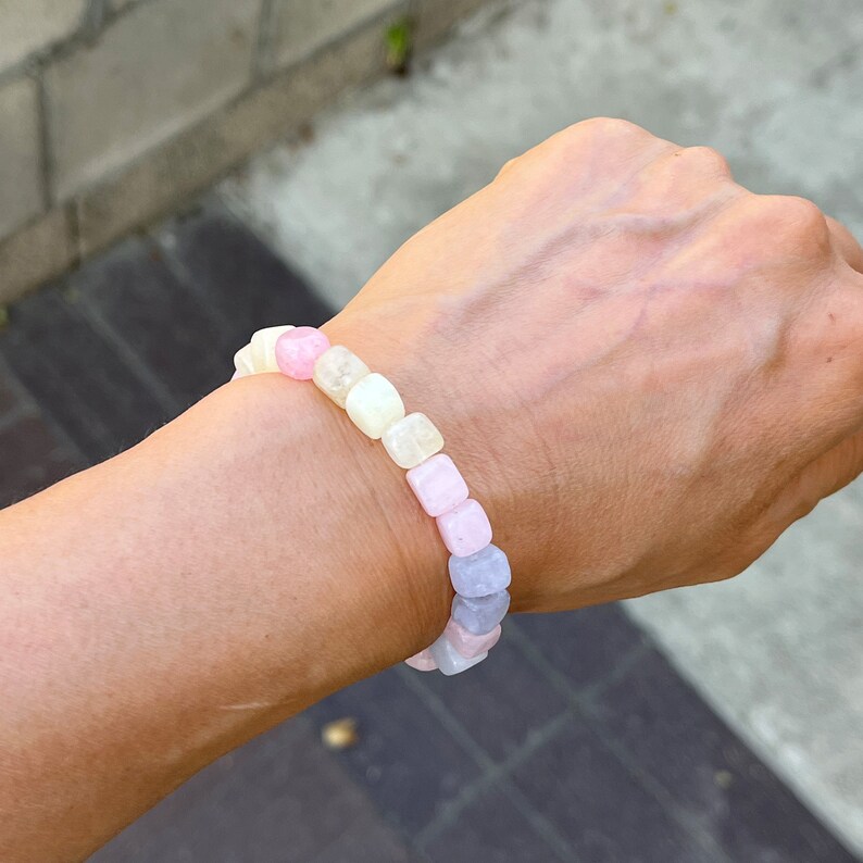 Peut inclure: Un bracelet aux couleurs pastel compos&eacute; de perles carr&eacute;es roses, jaunes et bleues. Le bracelet est port&eacute; au poignet, mettant en valeur le design et la palette de couleurs. Les perles semblent &ecirc;tre faites d'un mat&eacute;riau translucide.