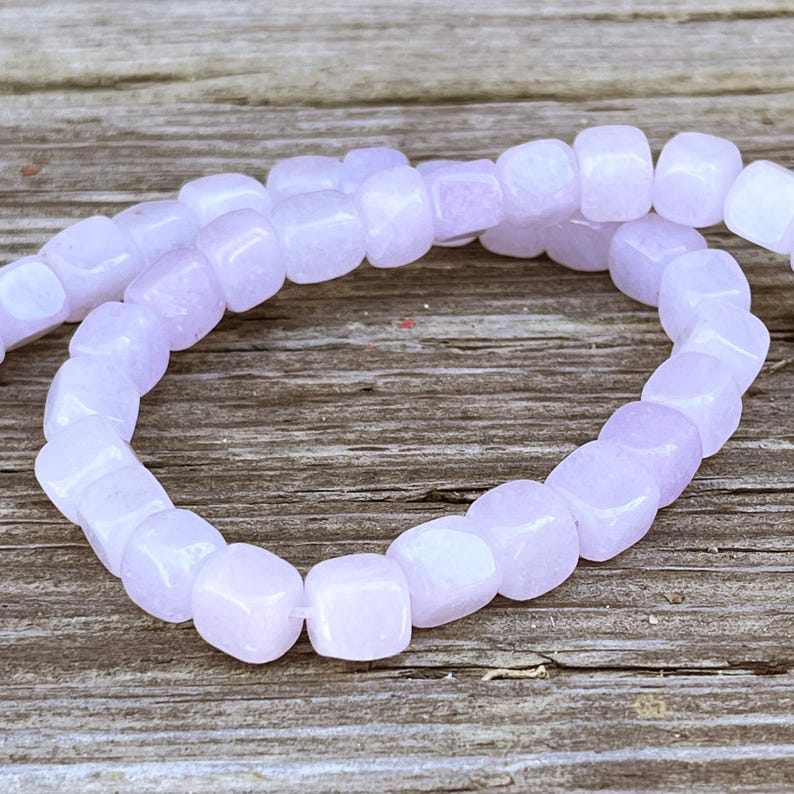 Pu&ograve; includere: Una fila di perline color viola chiaro a forma di cubo disposte in un motivo circolare. Ogni perlina presenta una superficie liscia e lucida con una tonalit&agrave; lavanda tenue e uniforme, infilate insieme per formare un anello continuo di componenti quadrati.