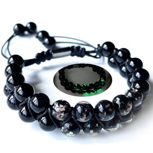 May include: Double-strand black beaded bracelet with a sliding knot closure. The beads have a glossy finish, with some beads featuring a speckled design. A smaller inset image shows the bracelet glowing green.